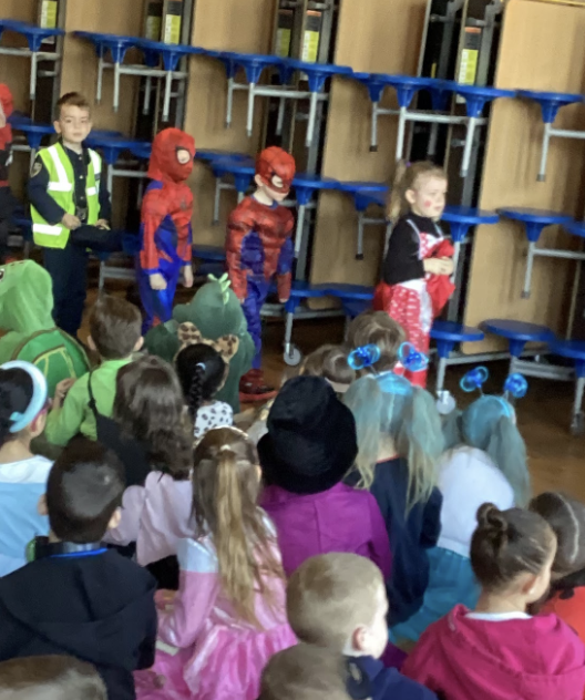 Students sat on the floor, watching students in costumes walking past in a line